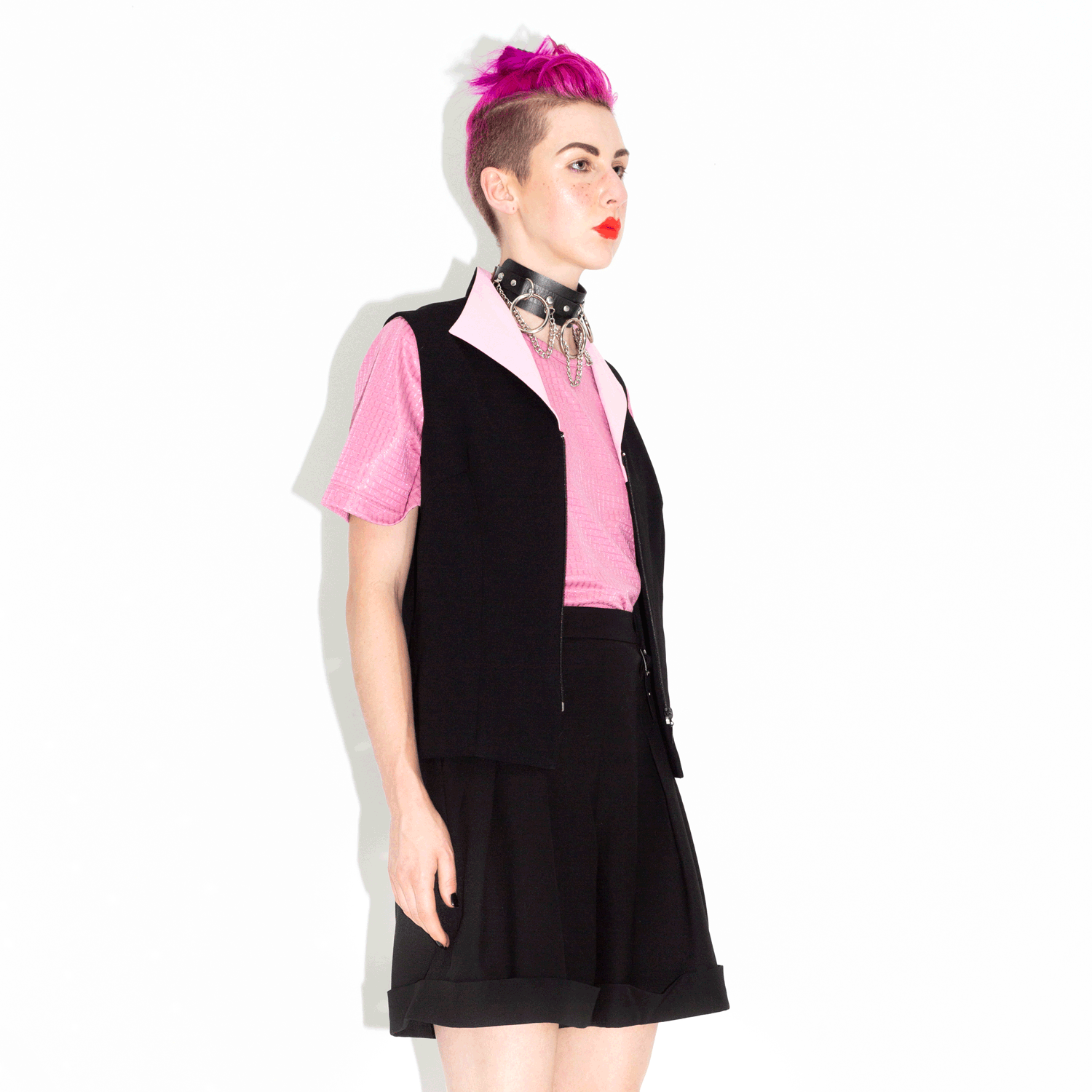 stop motion spinning model with edgy pink haircut wears pink shirt with black vest, black shorts, and chain choker collar